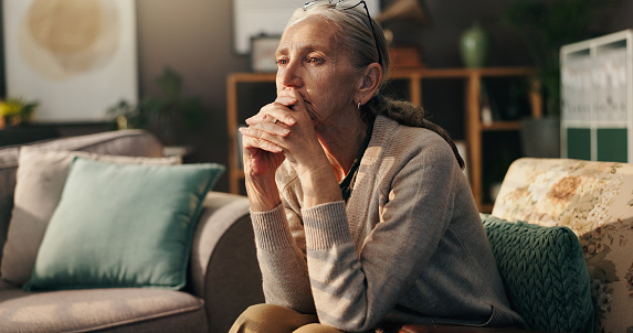 Woman in her home sitting on her couch. She is suffering from depression, a mental health condition, and looks sad and concerned.