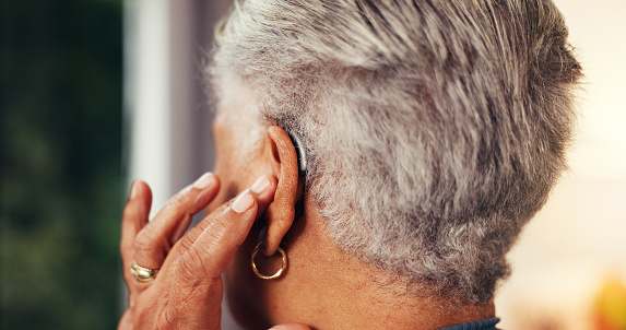 View of a woman from behind as she touches her ear to adjust her hearing aid.