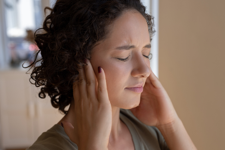 Female holding her ears and experiencing pain in the ear due to tinnitus